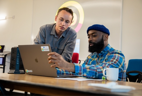 Two craftsperson in the London office chatting about code in front of a laptop